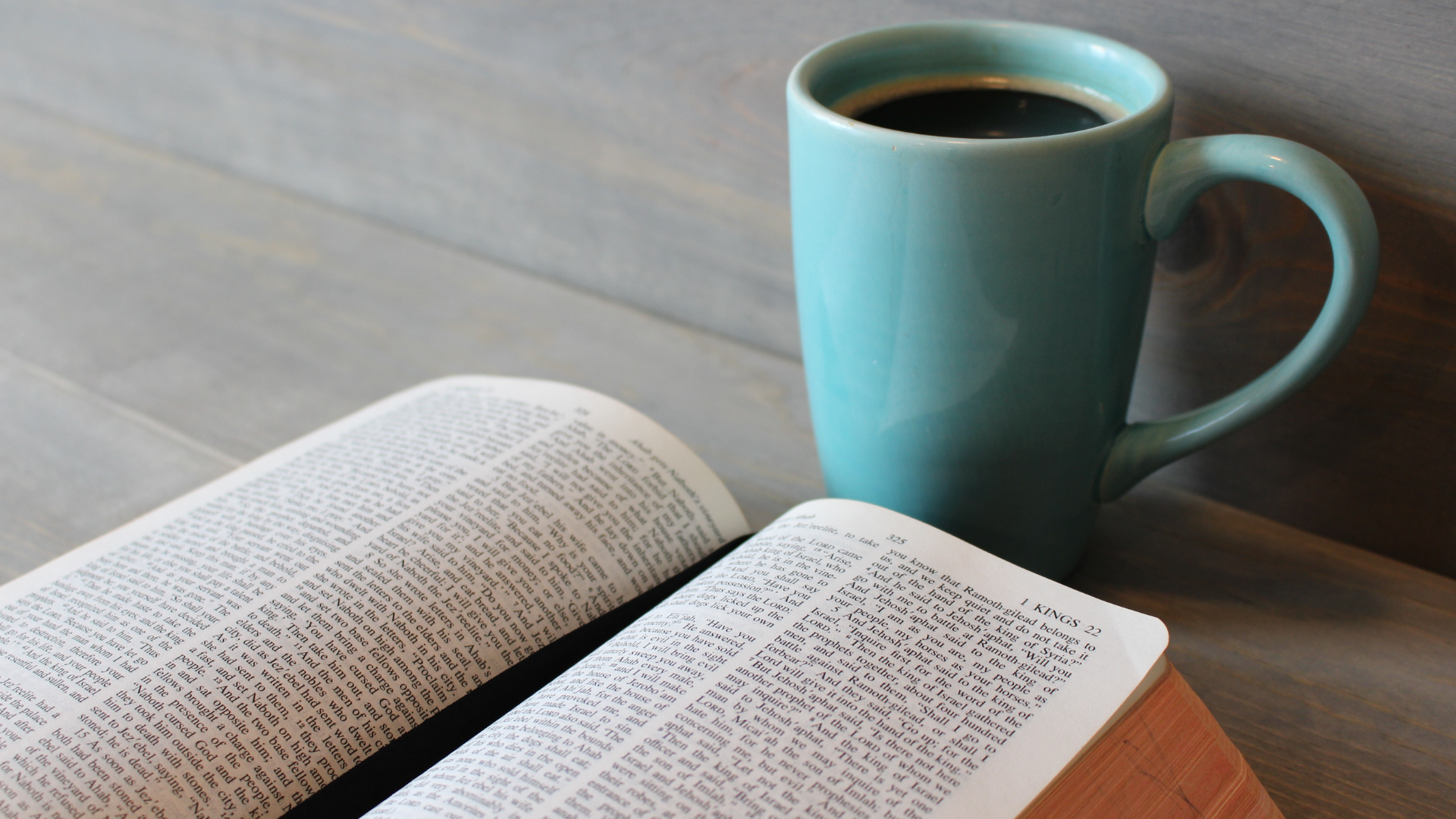 Bible open on table with blue mug of coffee
